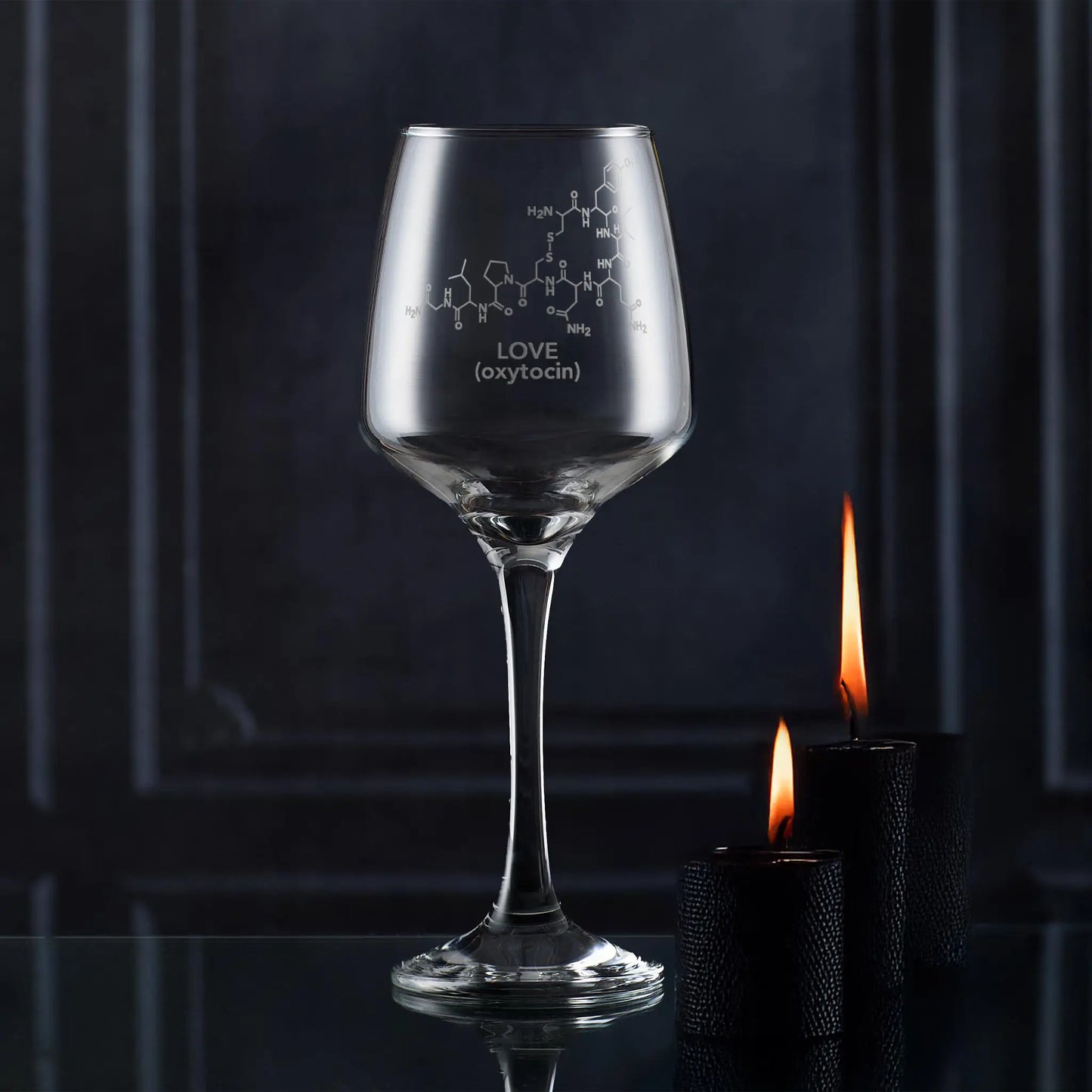 Wine glass with molecular design and 'LOVE (oxytocin)' text, lit by candles against a dark background