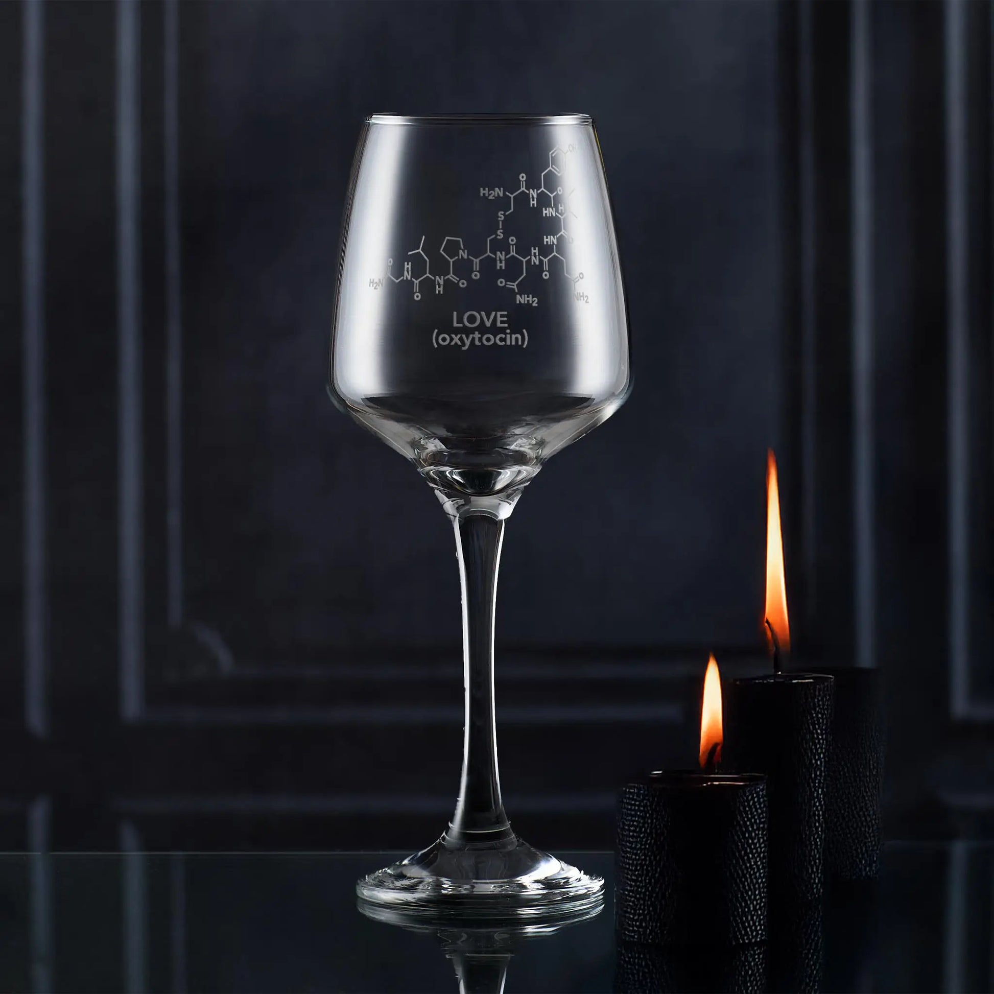 Wine glass with molecular design and 'LOVE (oxytocin)' text, lit by candles against a dark background
