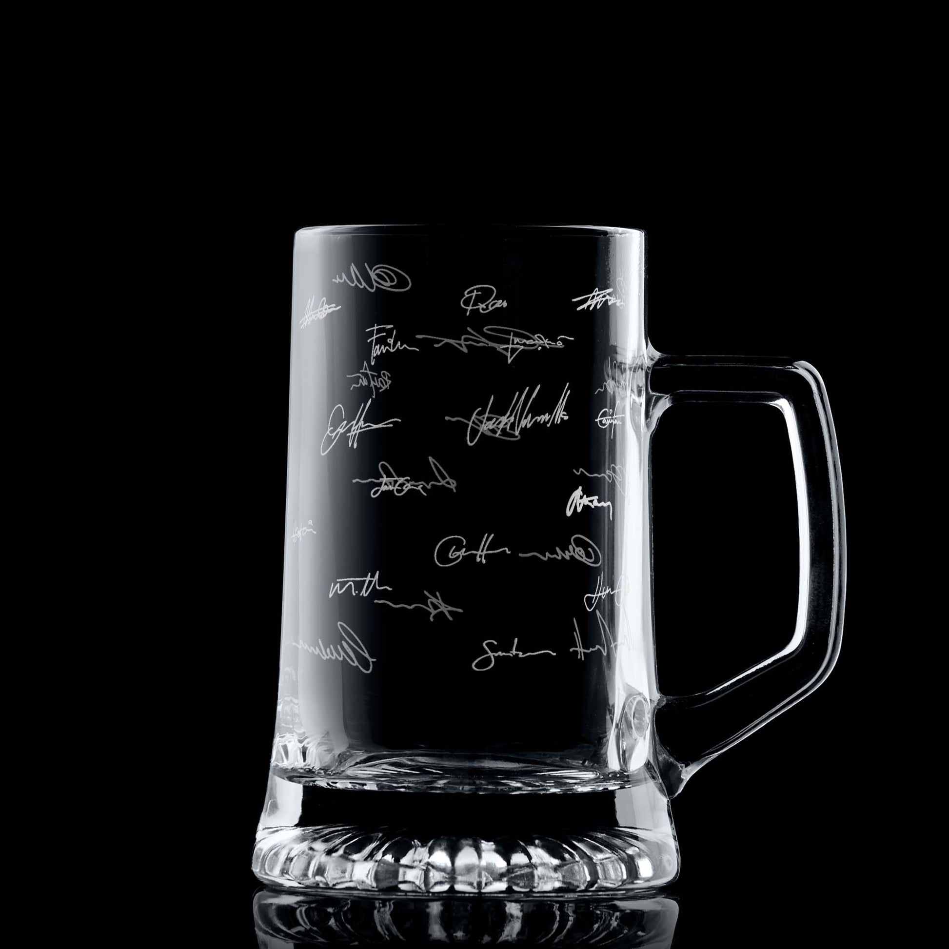 Glass beer tankard with engraved handwritten signatures on a black background