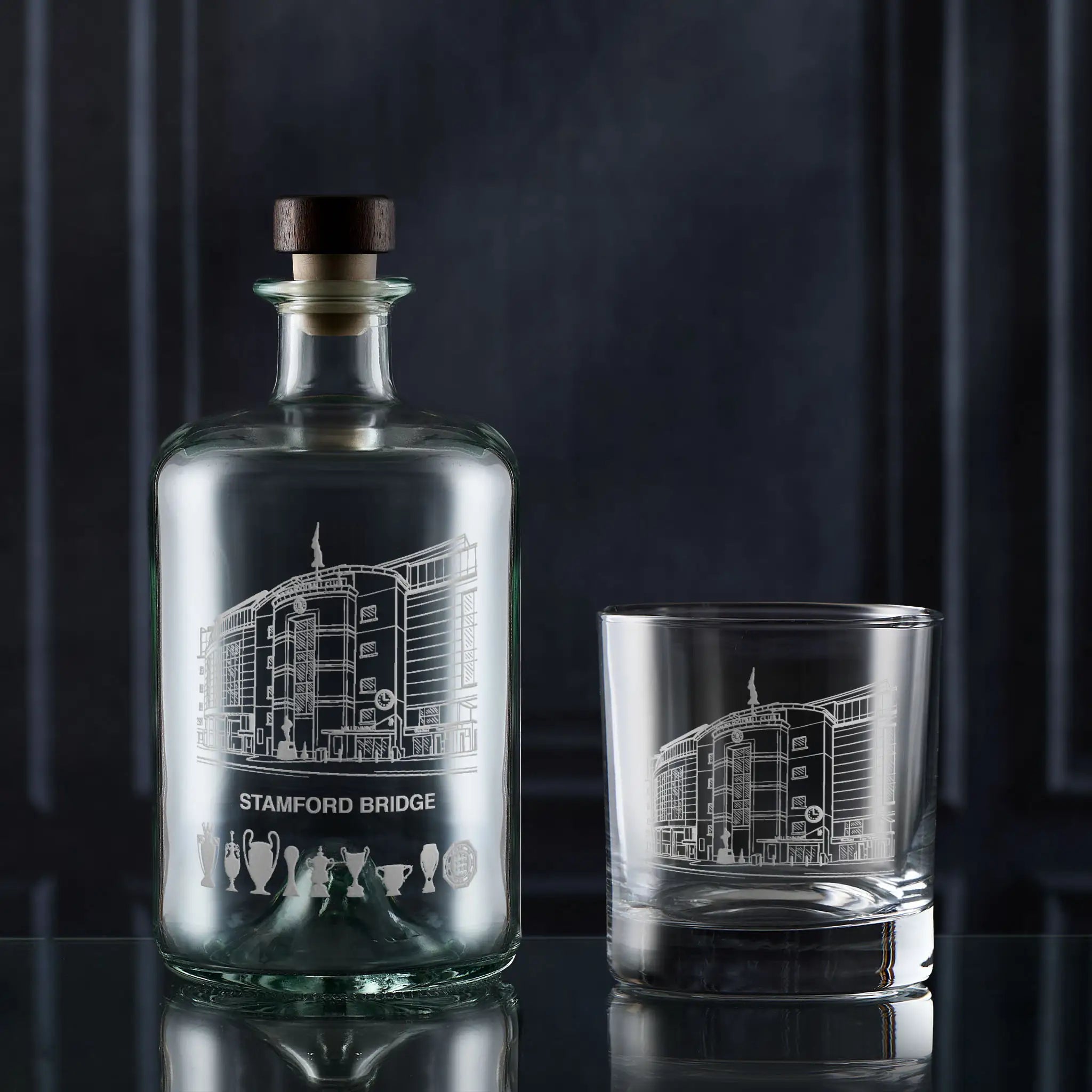 Glass decanter and glass with engraved design of Stamford Bridge stadium on a dark background