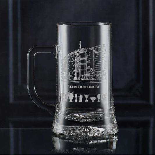 Engraved Stamford Bridge football stadium tankard shown on a dark panelled background with trophy silhouettes.