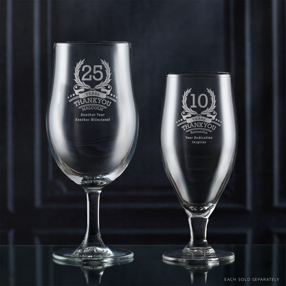 Two engraved corporate recognition glassware items on a reflective surface with a dark background