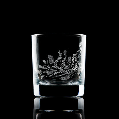 Side-view of engraved whisky glass featuring a flowing peacock tail with feathers and trailing leaves, inspired by Pittencrieff Park’s flora