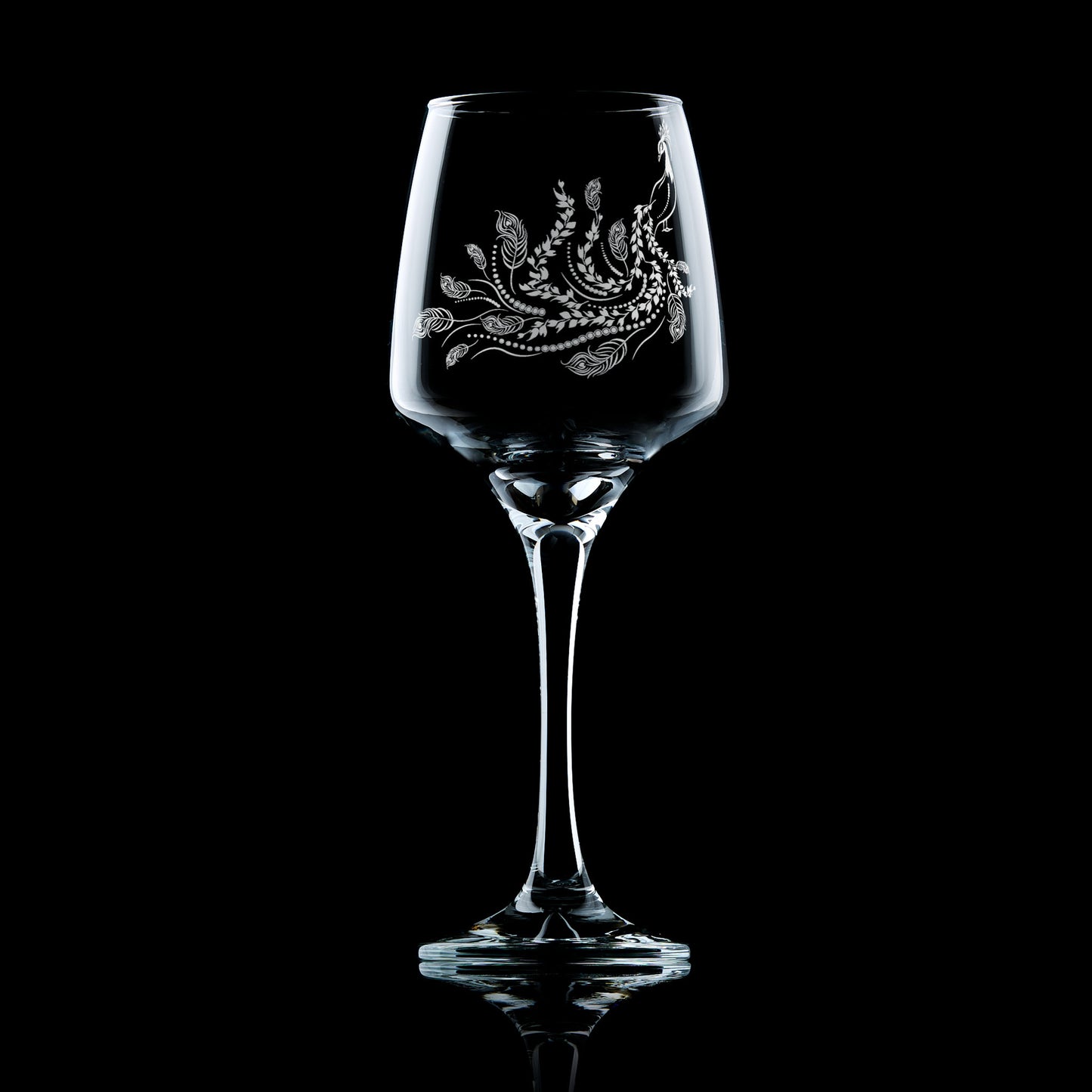 Front-view of engraved wine glass featuring a peacock with flowing tail of feathers and trailing leaves, inspired by Pittencrieff Park’s flora