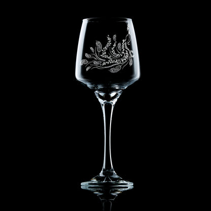 Front-view of engraved wine glass featuring a peacock with flowing tail of feathers and trailing leaves, inspired by Pittencrieff Park’s flora