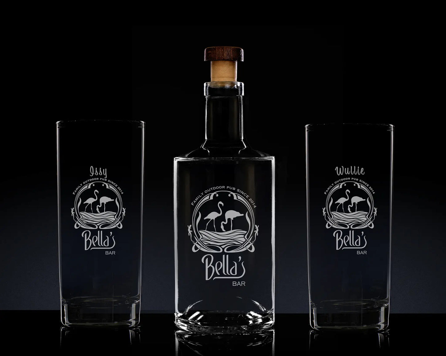 Bella's Bar bottle and two glasses with engraved designs on a dark background