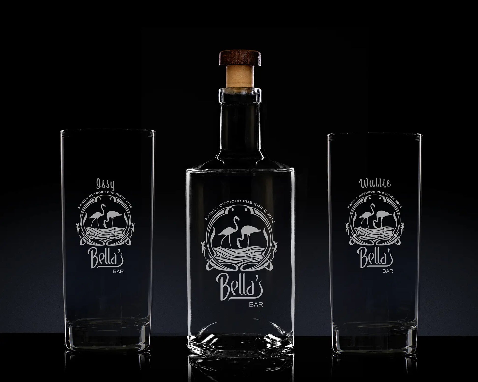 Bella's Bar bottle and two glasses with engraved designs on a dark background