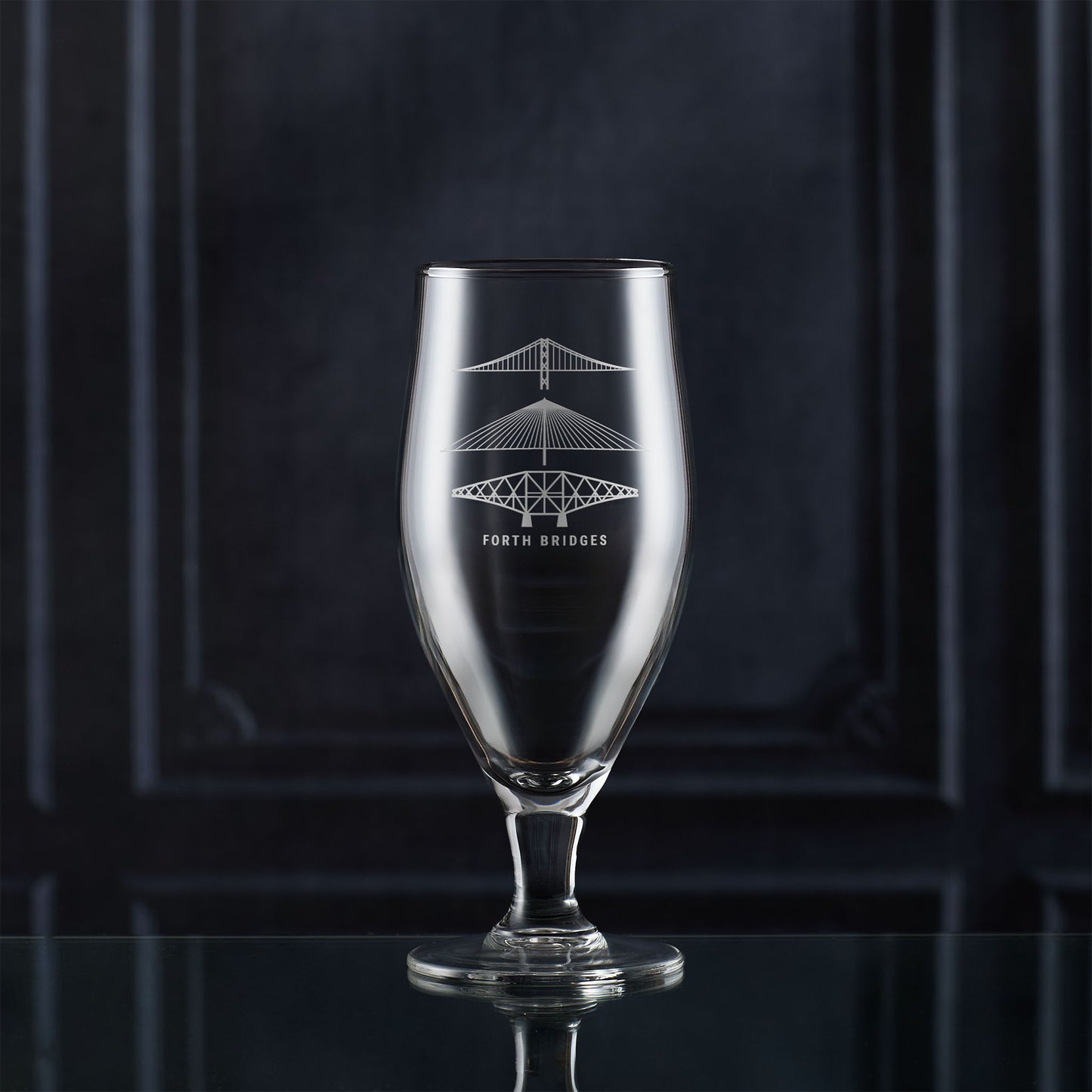 Stemmed beer glass with engraved scottish bridge design on a dark background