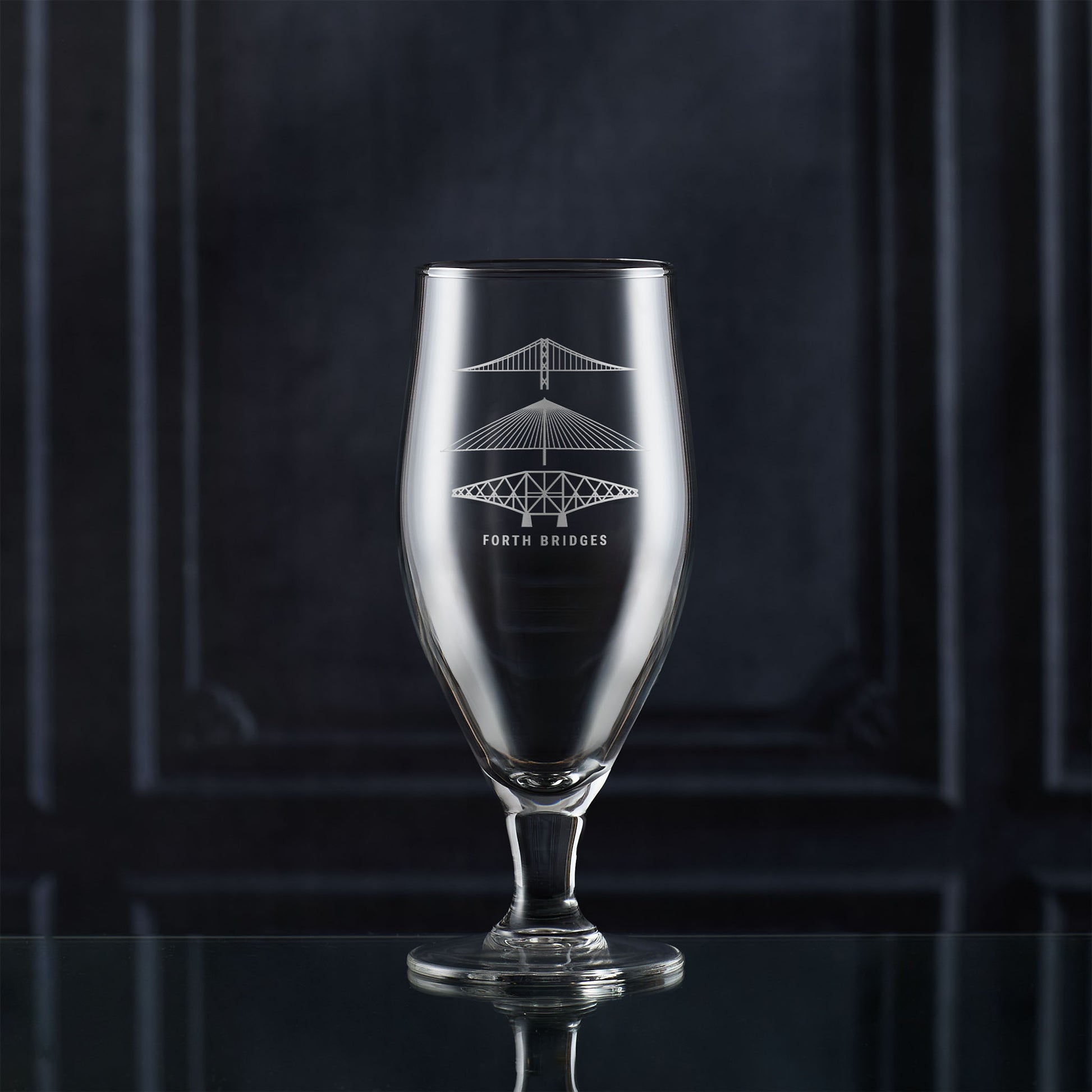 Stemmed beer glass with engraved scottish bridge design on a dark background