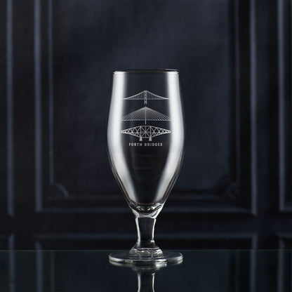 Stemmed beer glass with engraved scottish bridge design on a dark background