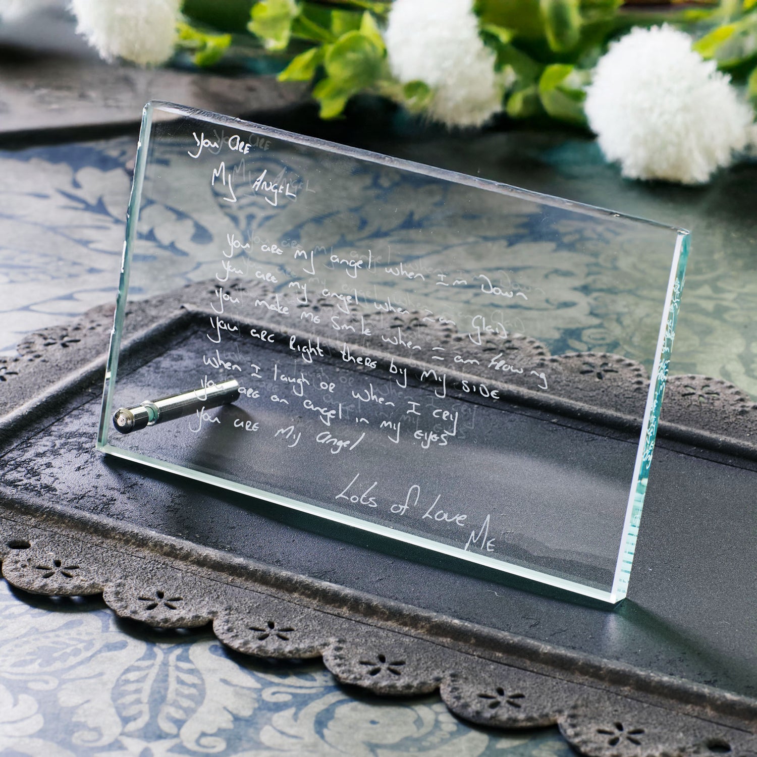Glass plaque with engraved handwritten text on a decorative tray with flowers in the background