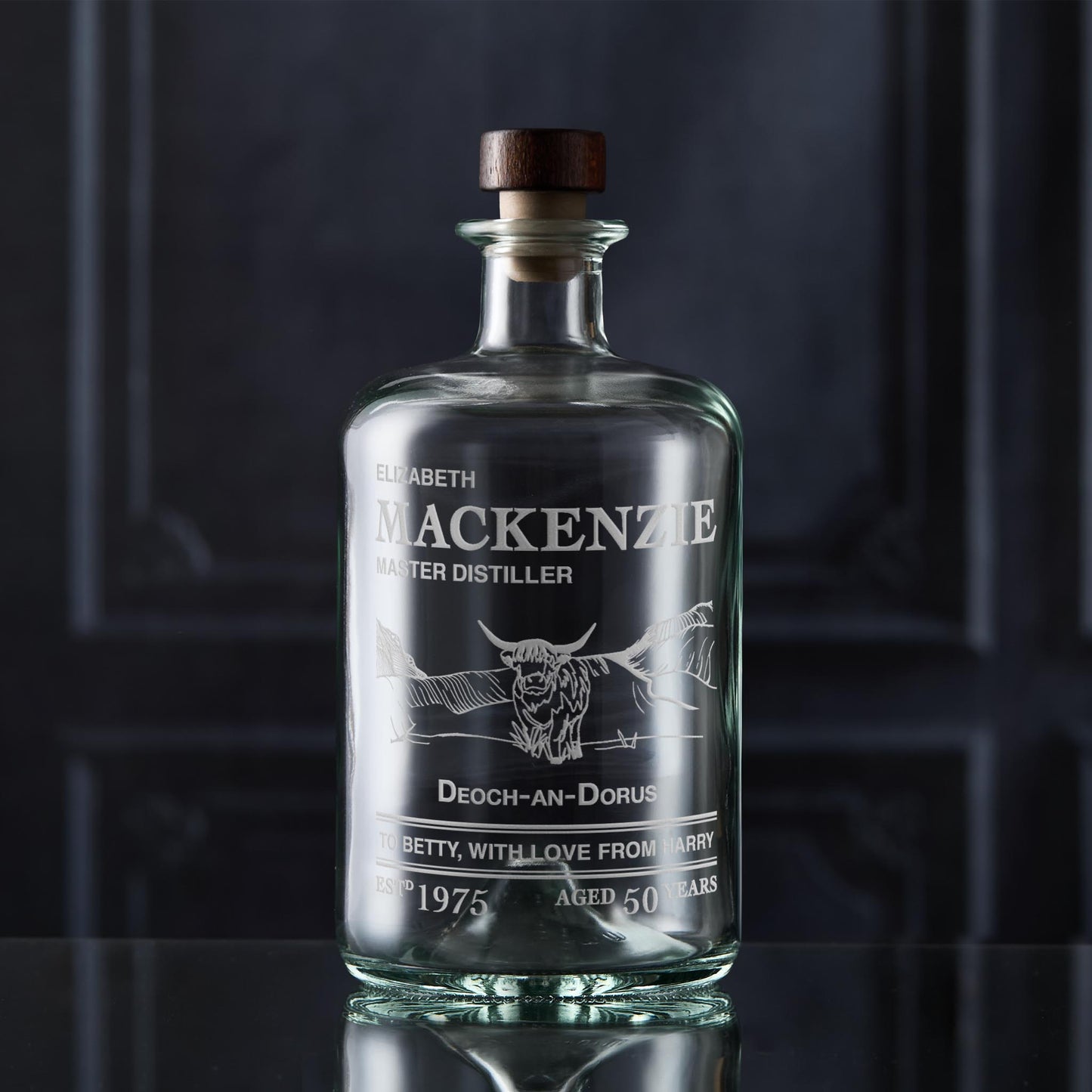 Glass decanter bottle engraved with a label featuring custom text and a Highland Coo 