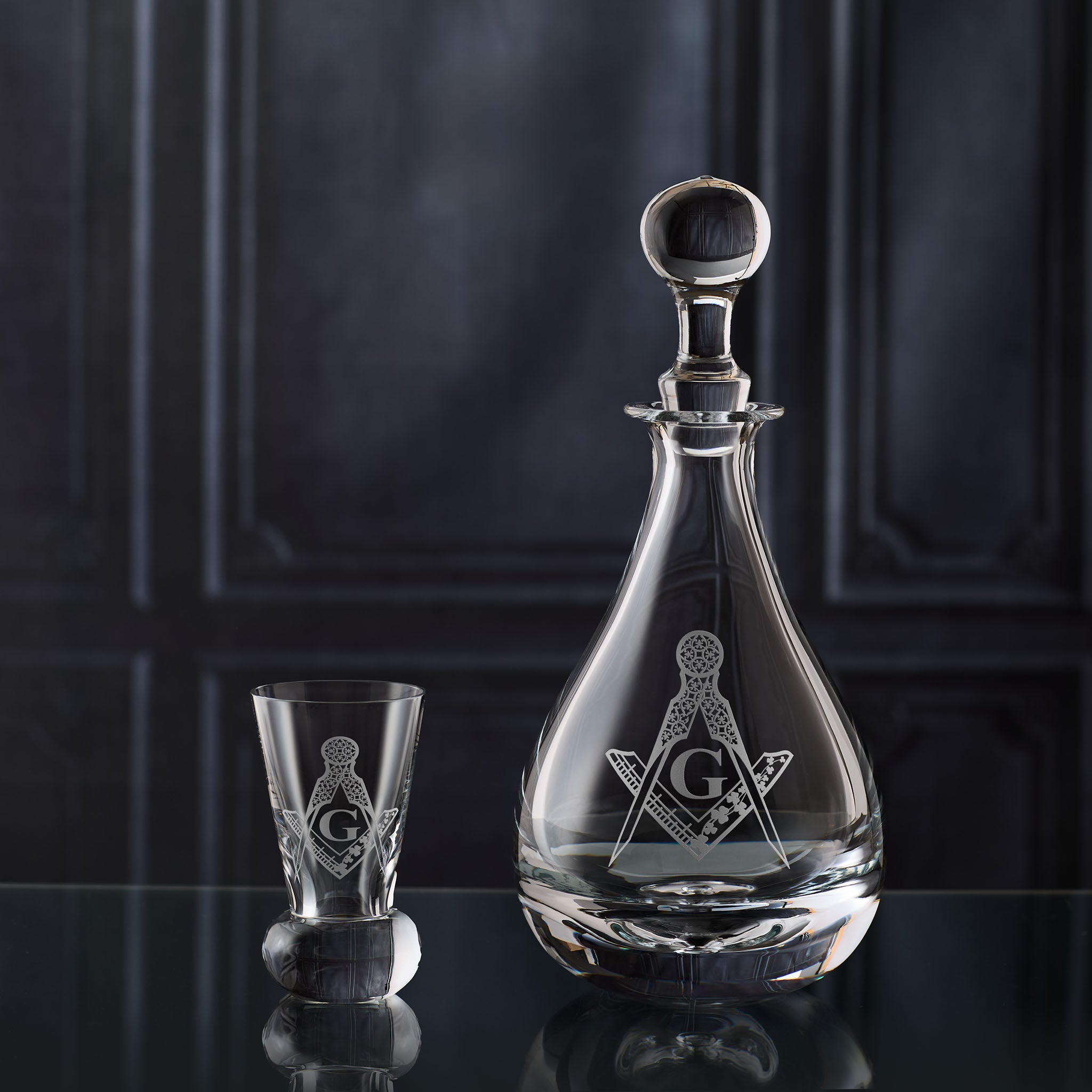 Glass decanter and firing glass engraved with Masonic symbols on a dark background