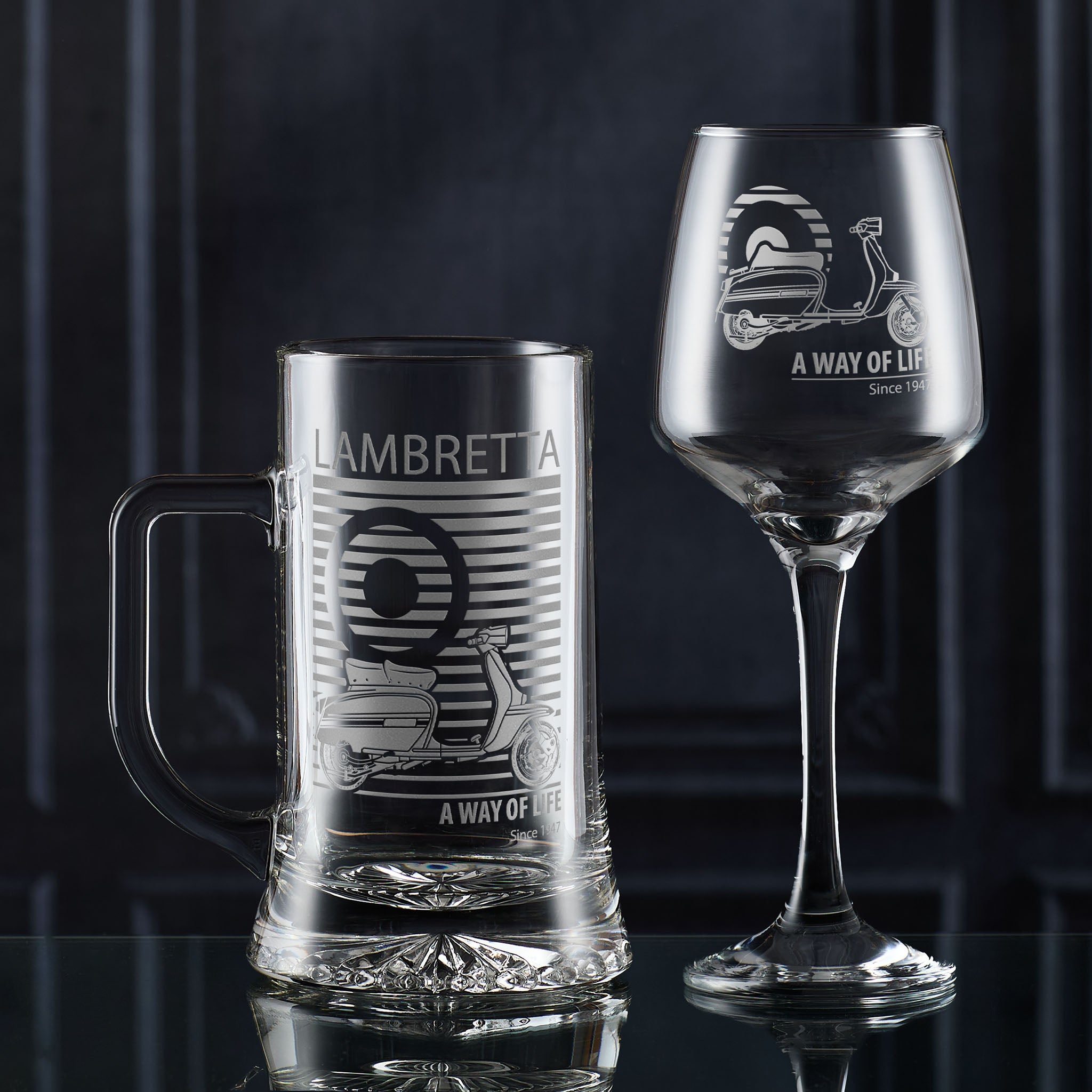 Clear glass mug and stemmed wine glass engraved Lambretta scooter design on a dark background