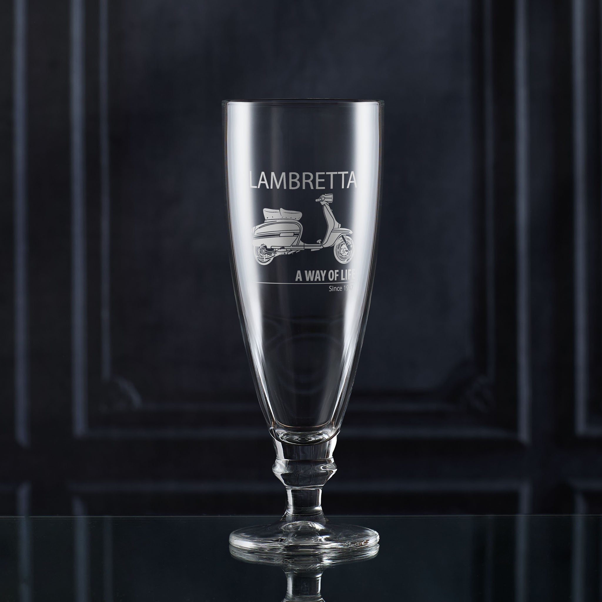 Clear stemmed beer glass with Lambretta scooter engraving on a dark background