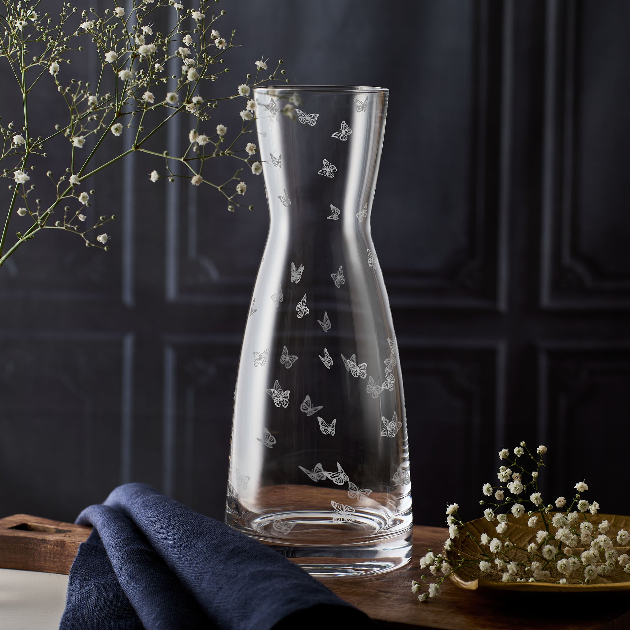 Clear glass carafe with butterfly designs on a dark background