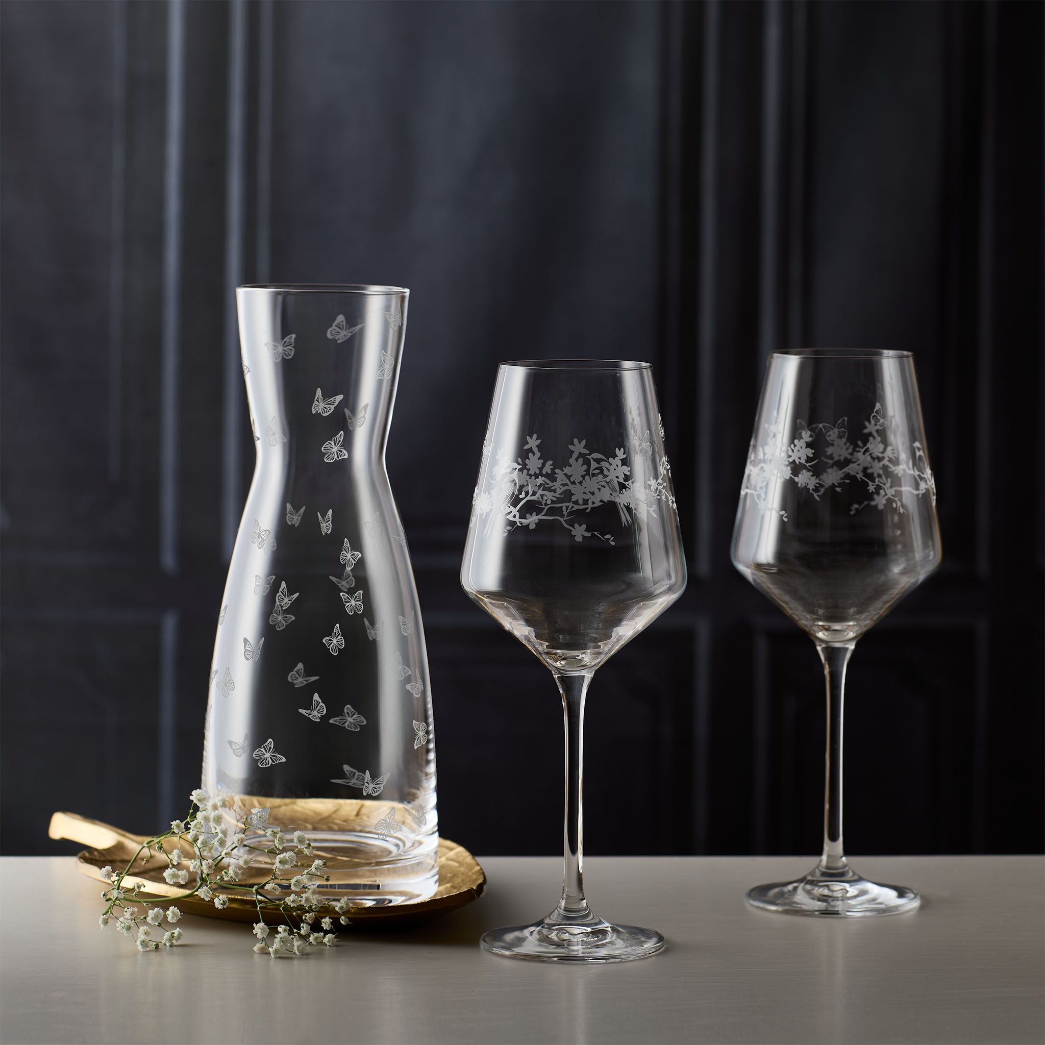 Set of glass carafe and wine glasses with engraved floral, bird and butterfly motifs on a dark background