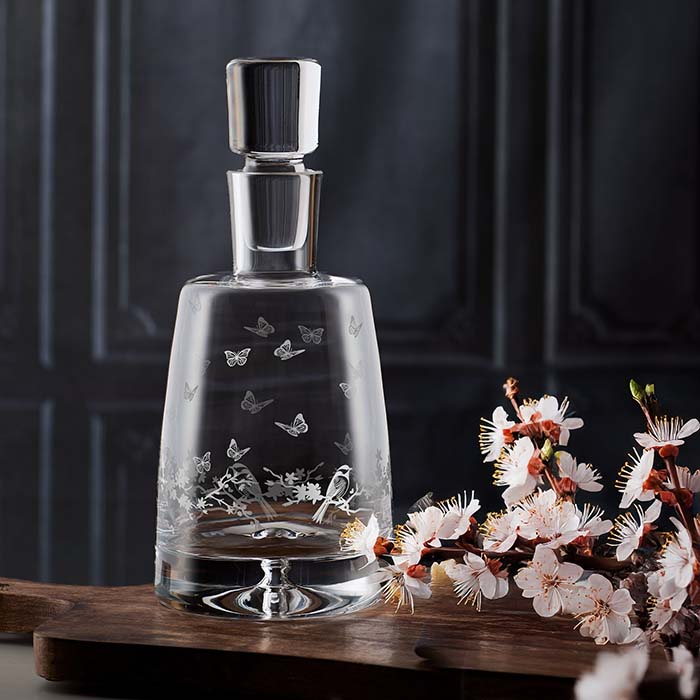 Glass decanter with butterfly designs on a wooden surface with flowers