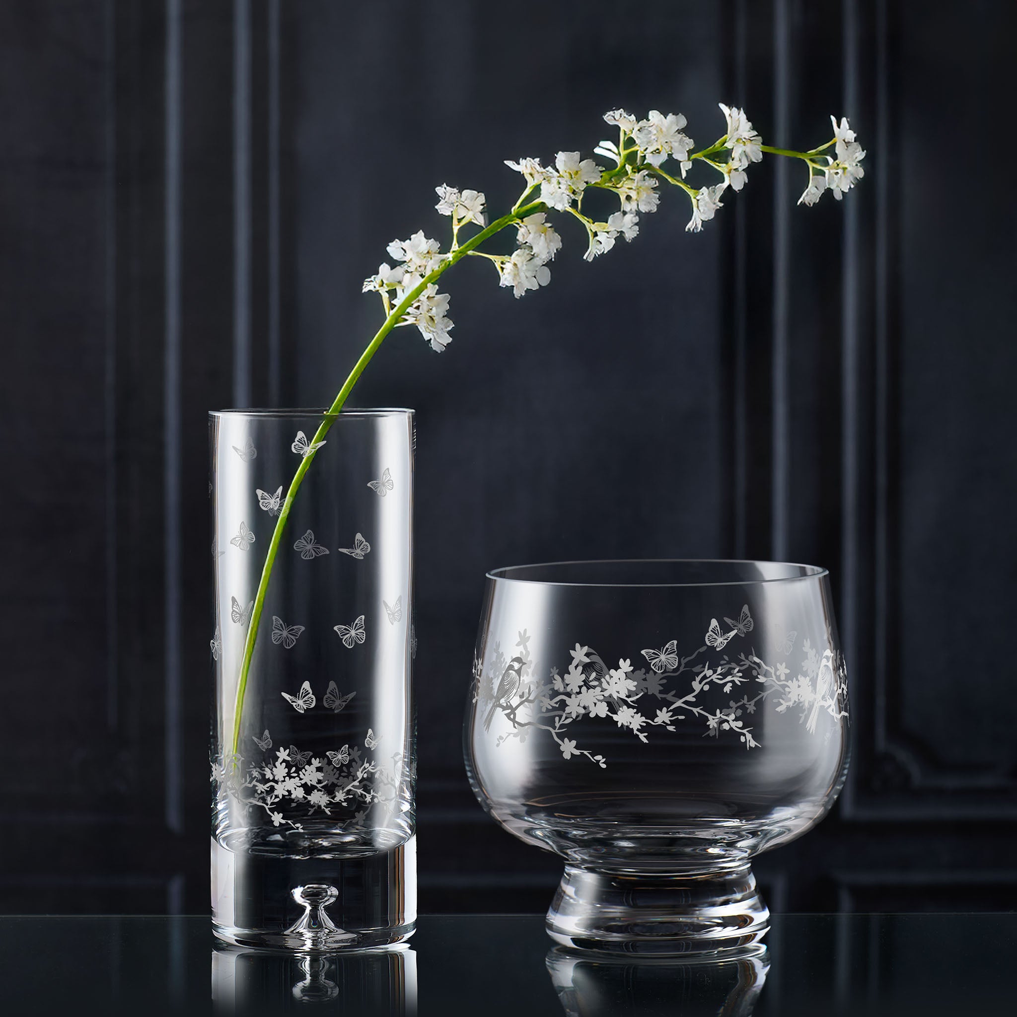Two glass vases with floral etchings on a dark background