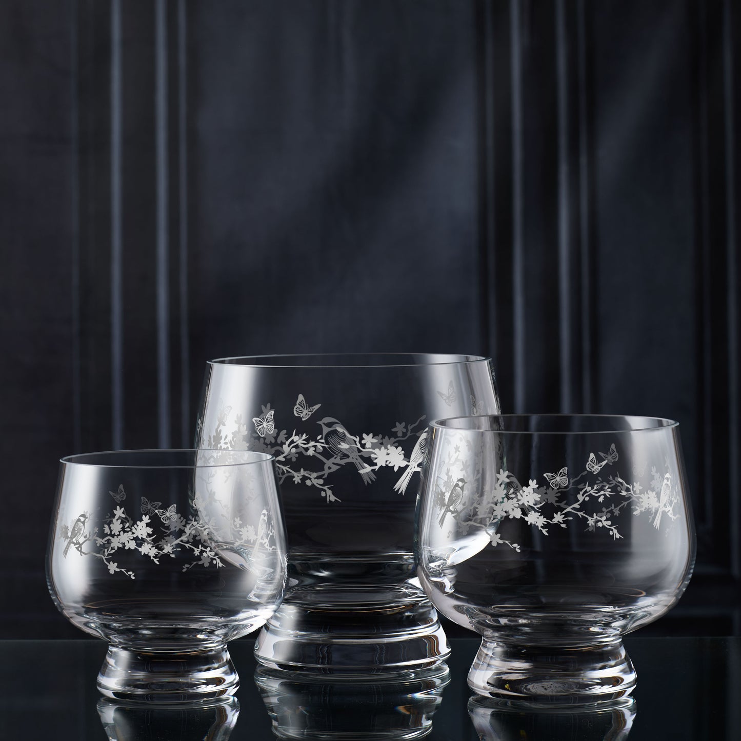 Three glass tulip bowls with floral engraving on a dark background
