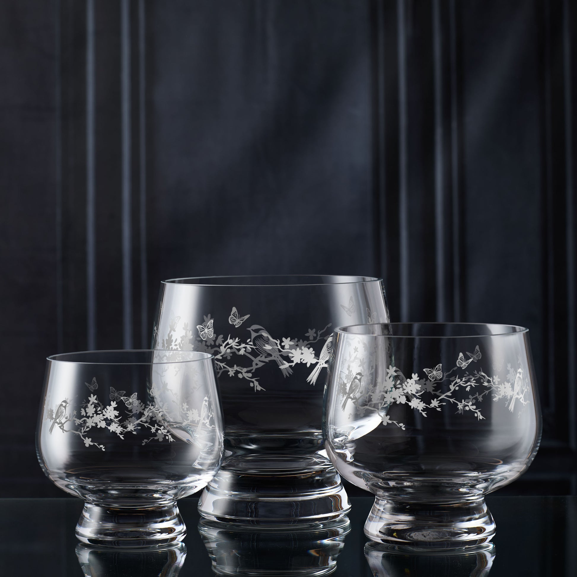 Three glass tulip bowls with floral engraving on a dark background