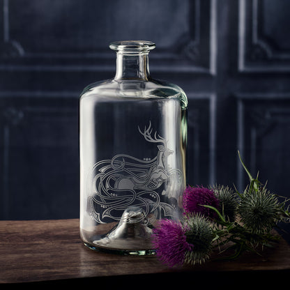 Whisky decanter with engraved celtic stag design on a wooden surface with purple flowers and greenery.
