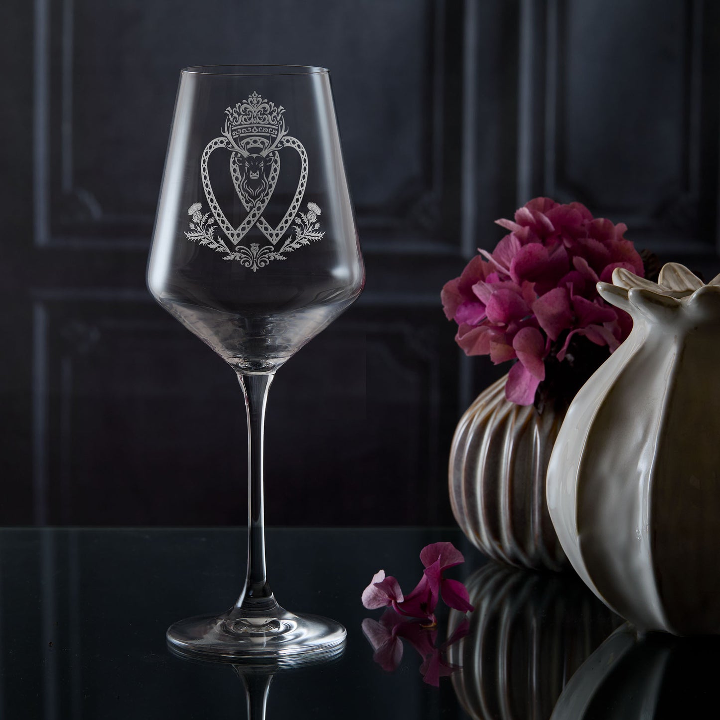 Decorative Luckenbooth wine glass with intricate heart design and scottish stag on a dark surface with flowers and a vase.