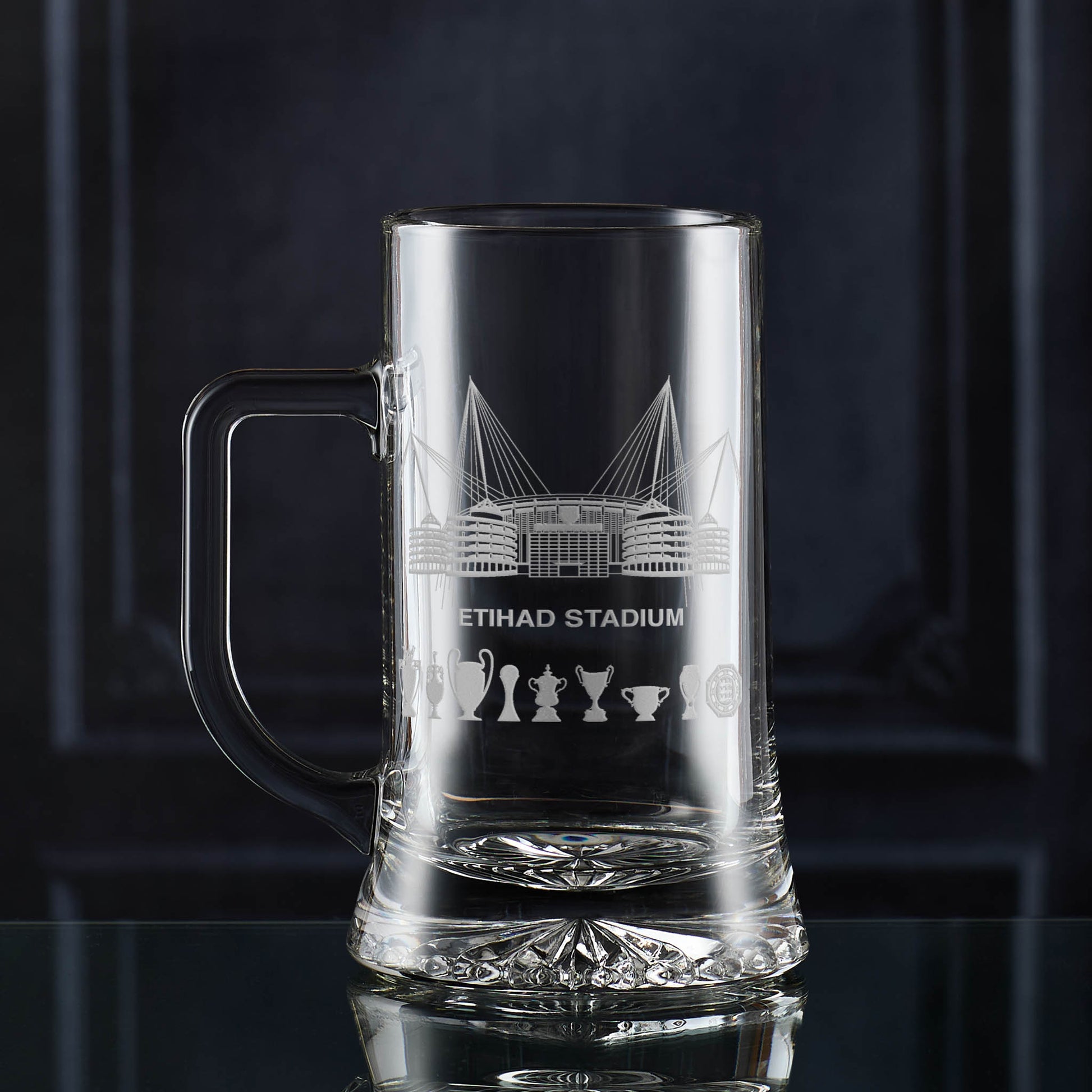 Hand-engraved tankard with Etihad Stadium artwork and symbolic trophy silhouettes, displayed against a dark background.