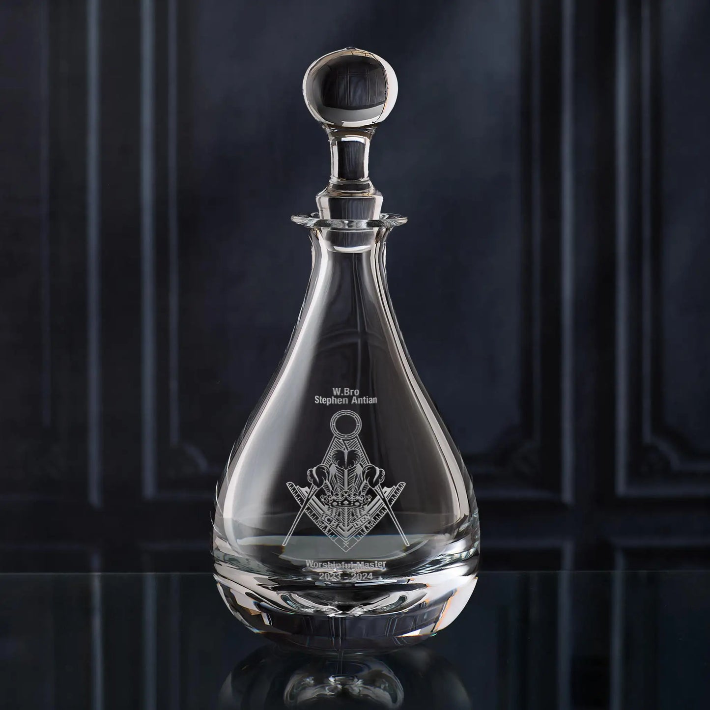 Clear glass wine decanter with Masonic lodge symbol on a dark background