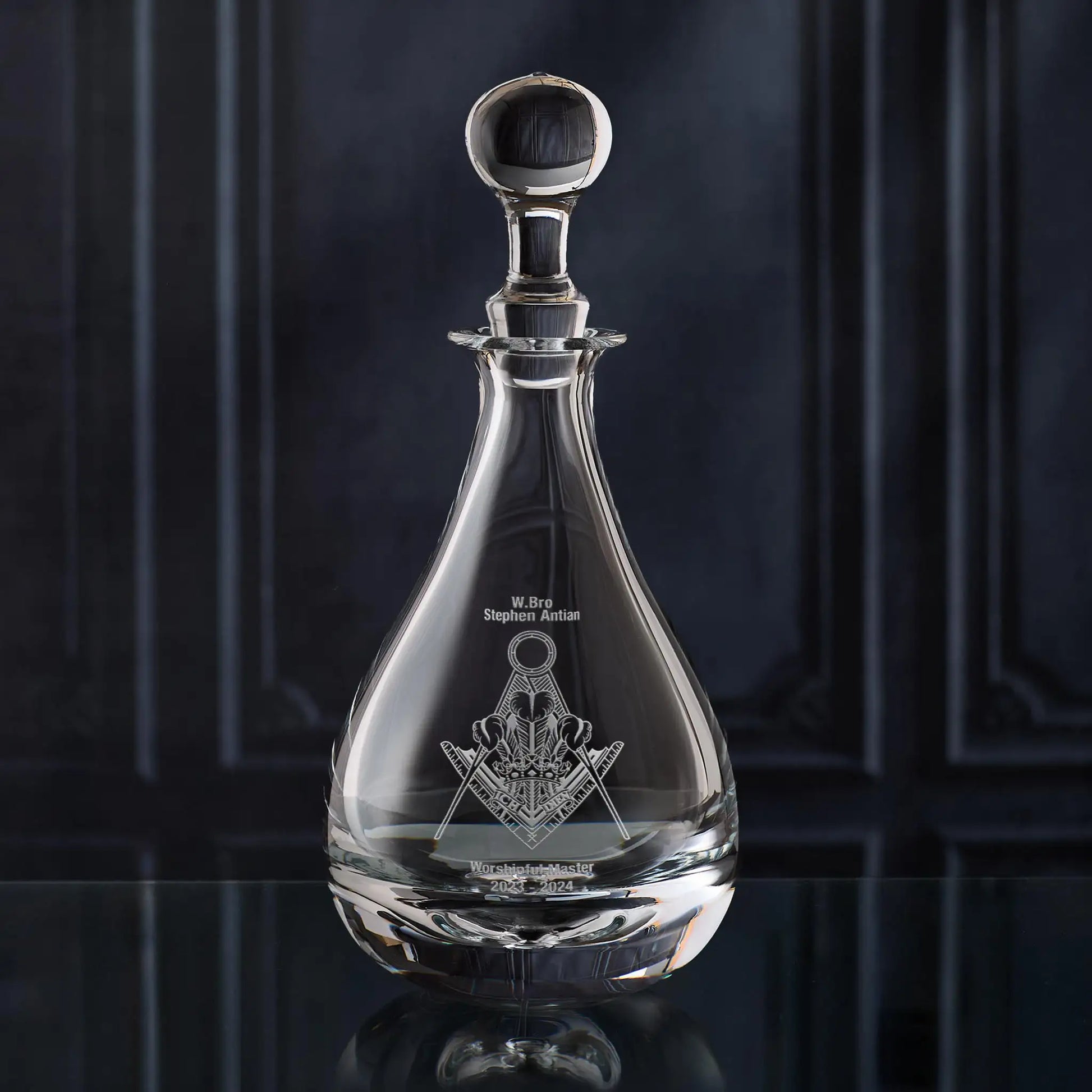 Clear glass wine decanter with Masonic lodge symbol on a dark background