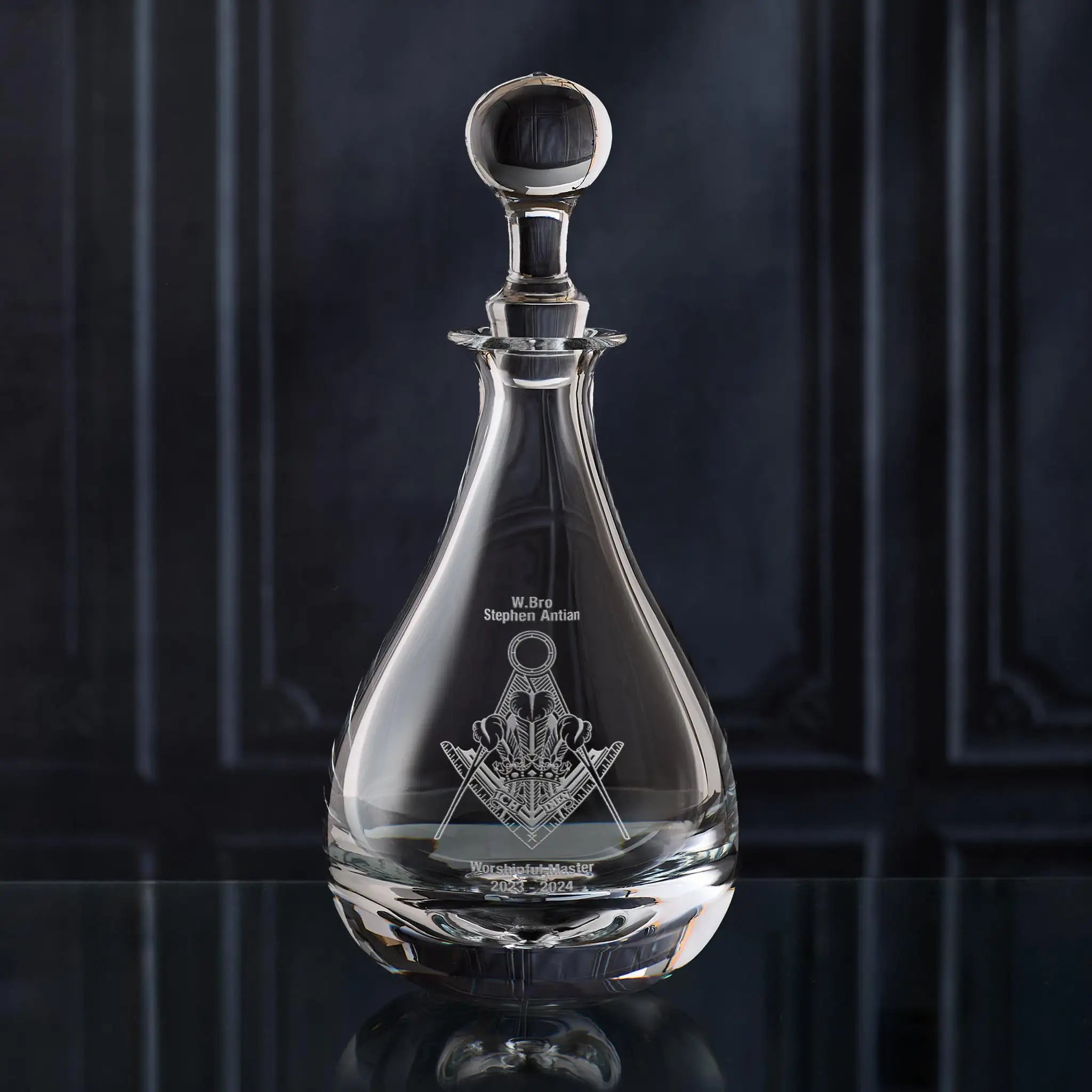 Clear glass wine decanter with Masonic lodge symbol on a dark background