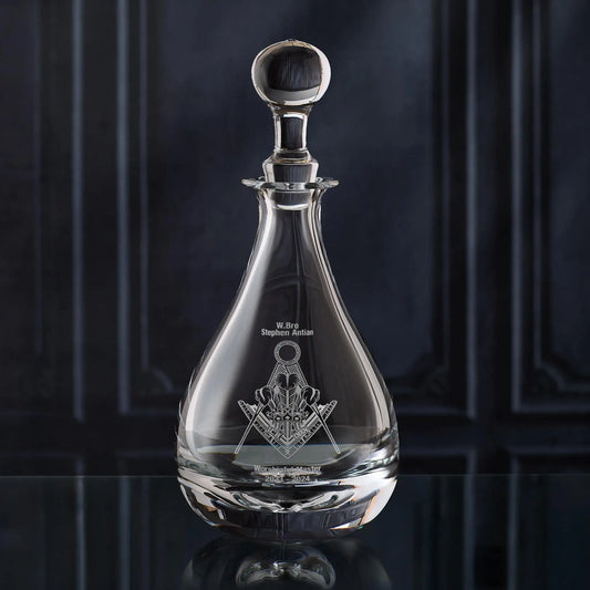 Clear glass wine decanter with Masonic lodge symbol on a dark background