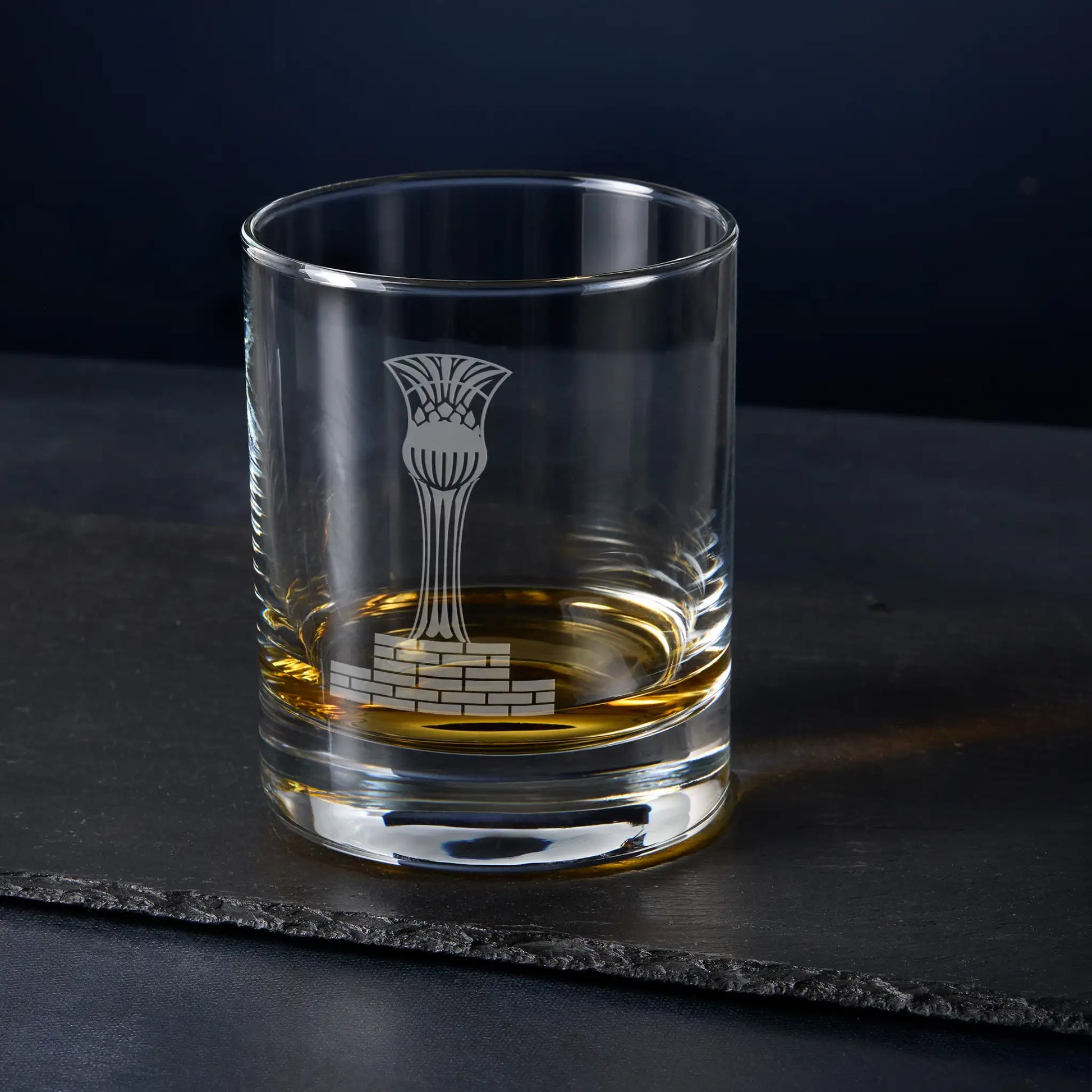 Clear glass tumbler with engraved masonic steward cup design on a dark surface