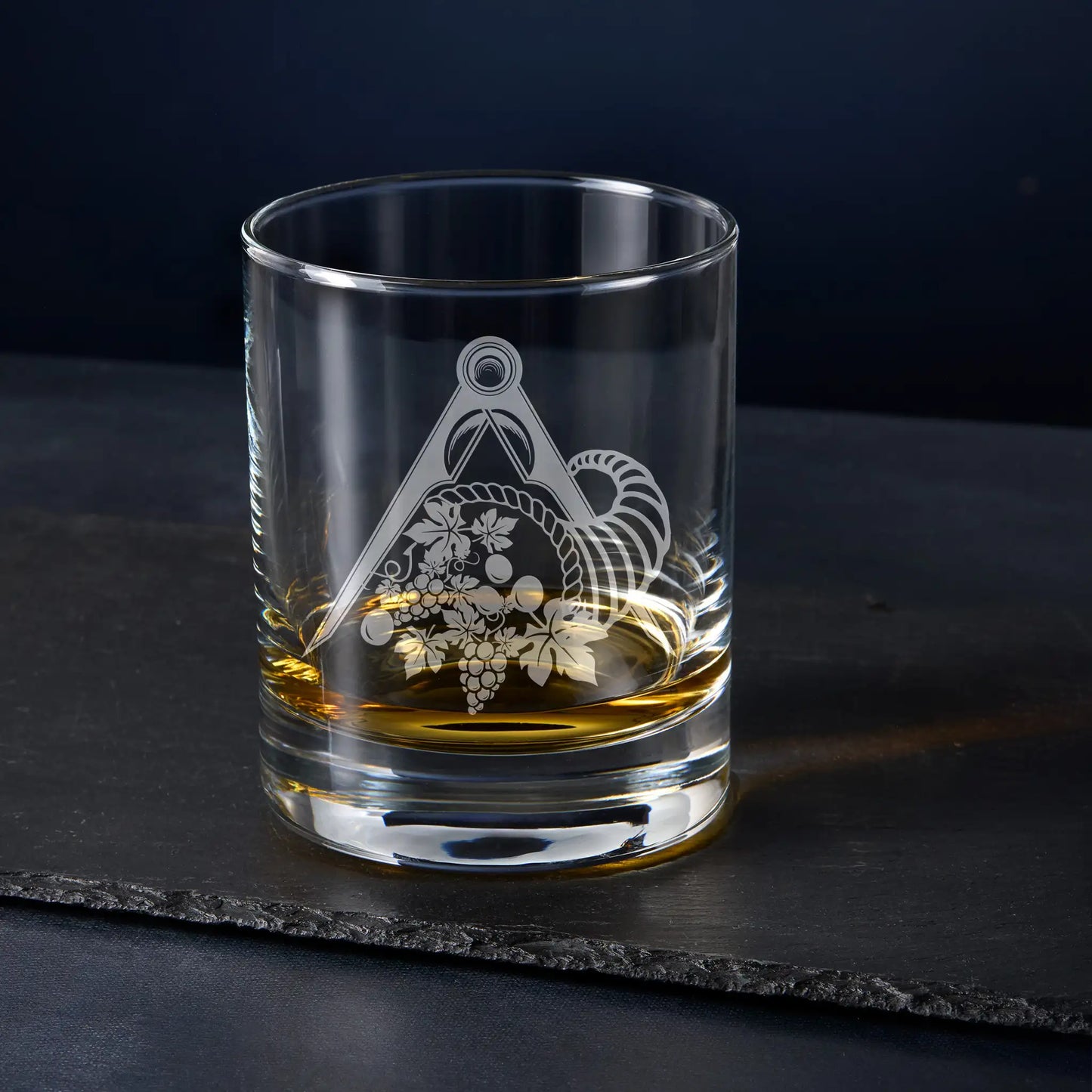 Engraved whisky glass with cornucopia symbol for Masonic Stewards, photographed on a dark textured backdrop