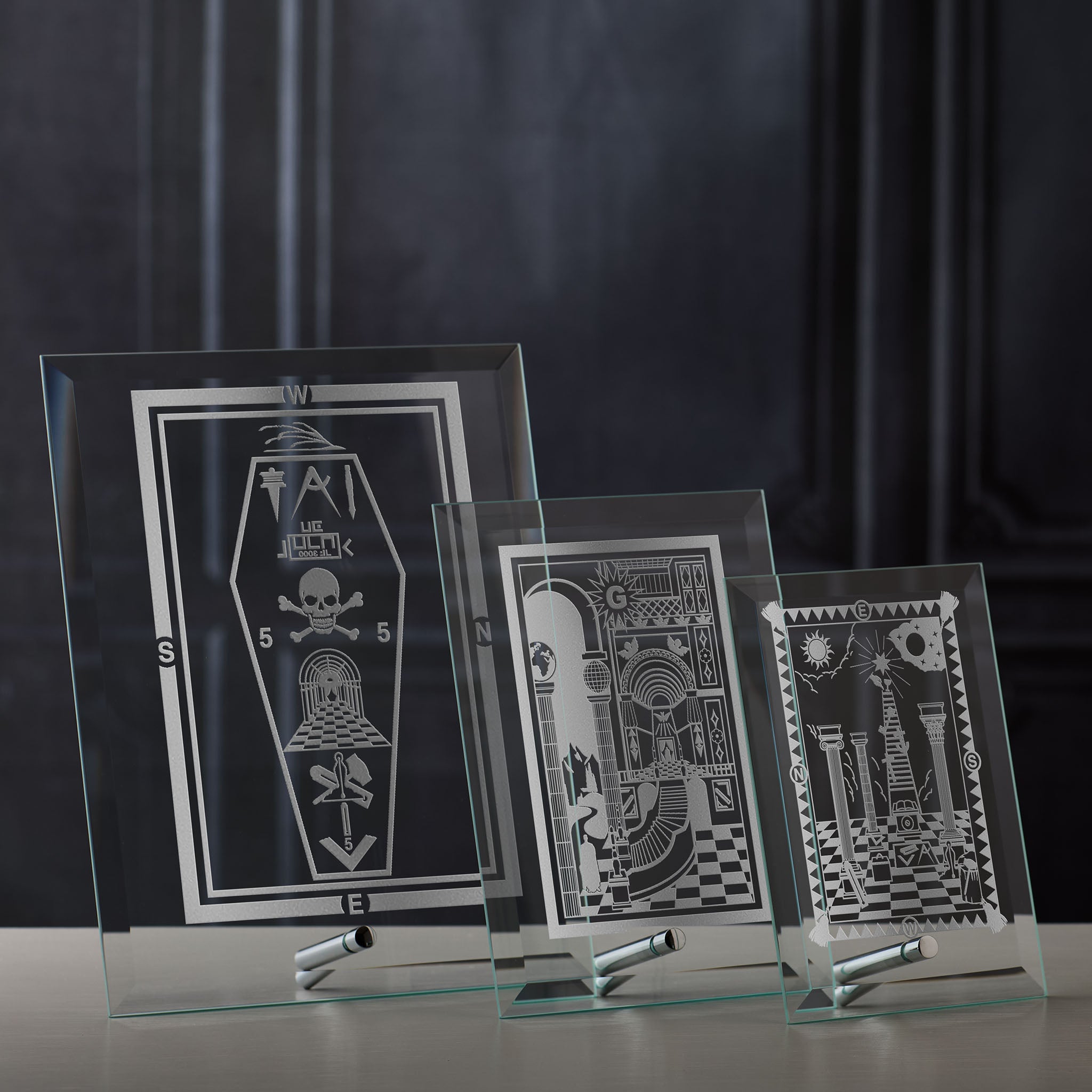 Three glass frames engraved with masonic tracing boards on a dark background