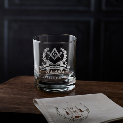 Whisky glass with Masonic design and engraved text on a wooden surface with a dark background