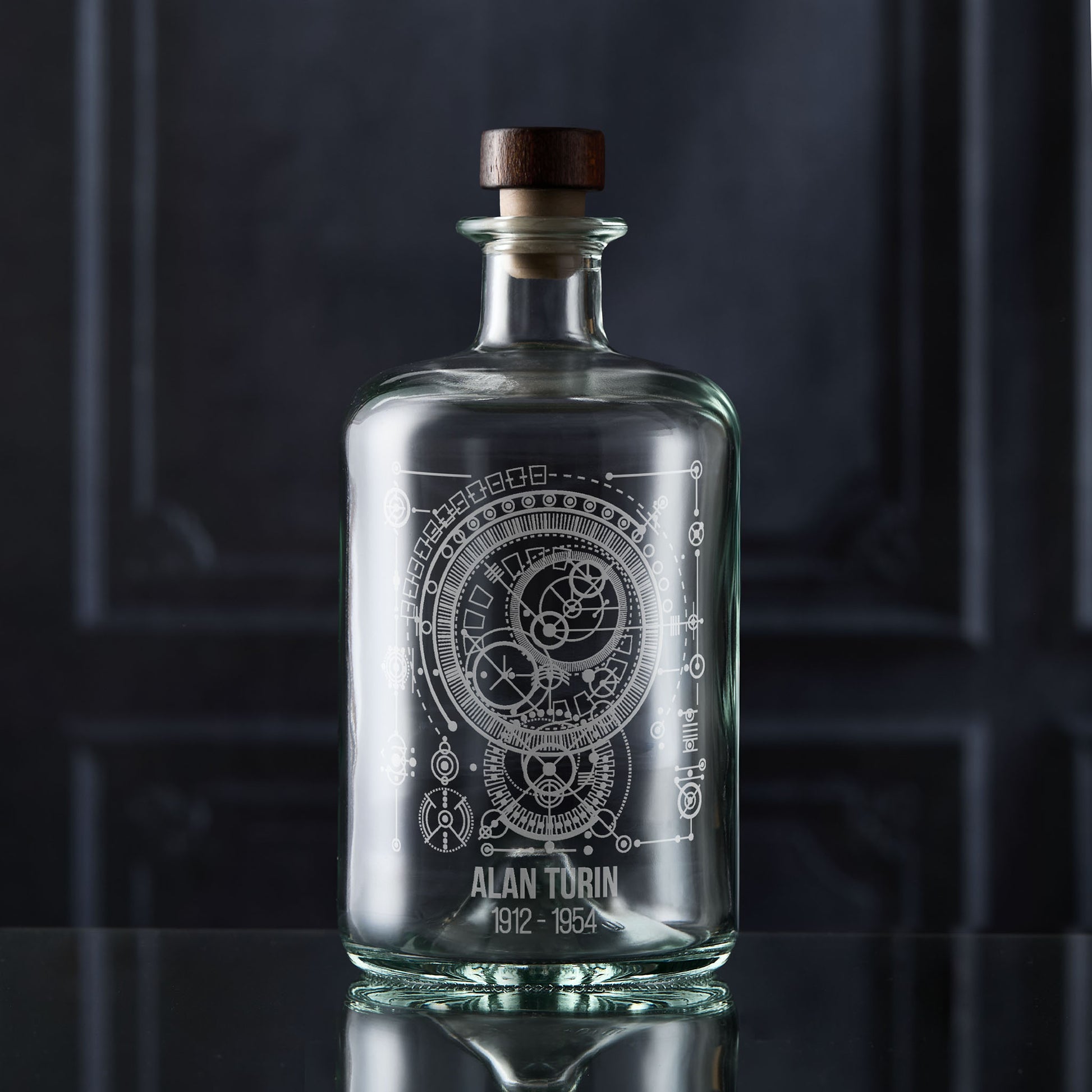 Clear glass decanter bottle with engraved maths design and wooden stopper on a dark background