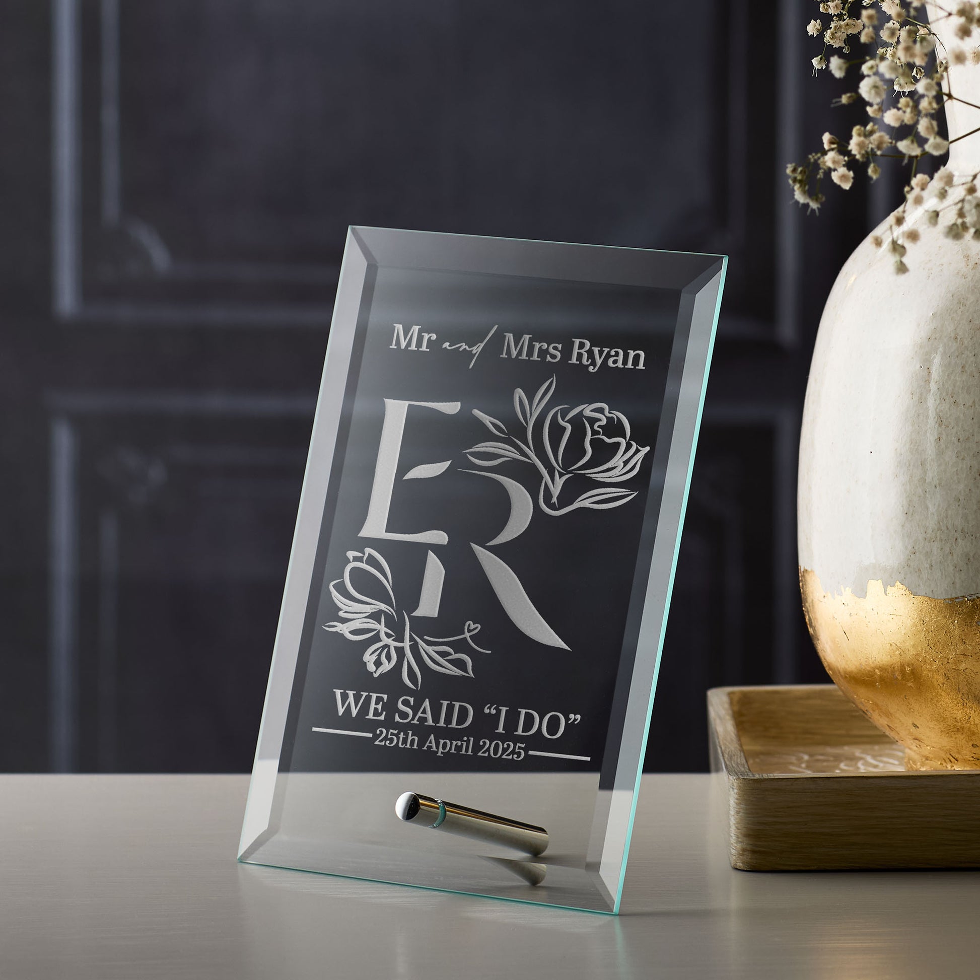 Personalized glass frame with engraved initials, wedding flowers and date on a dark background