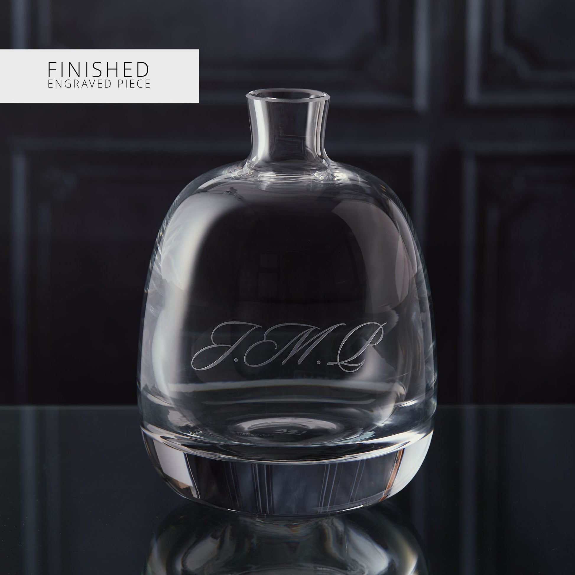 Clear glass decanter with engraved text on a dark background
