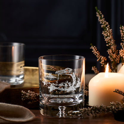 Loch Ness whisky glass with engraved Nessie design on a table with a candle and decorative elements