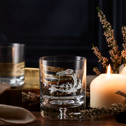 Loch Ness whisky glass with engraved Nessie design on a table with a candle and decorative elements
