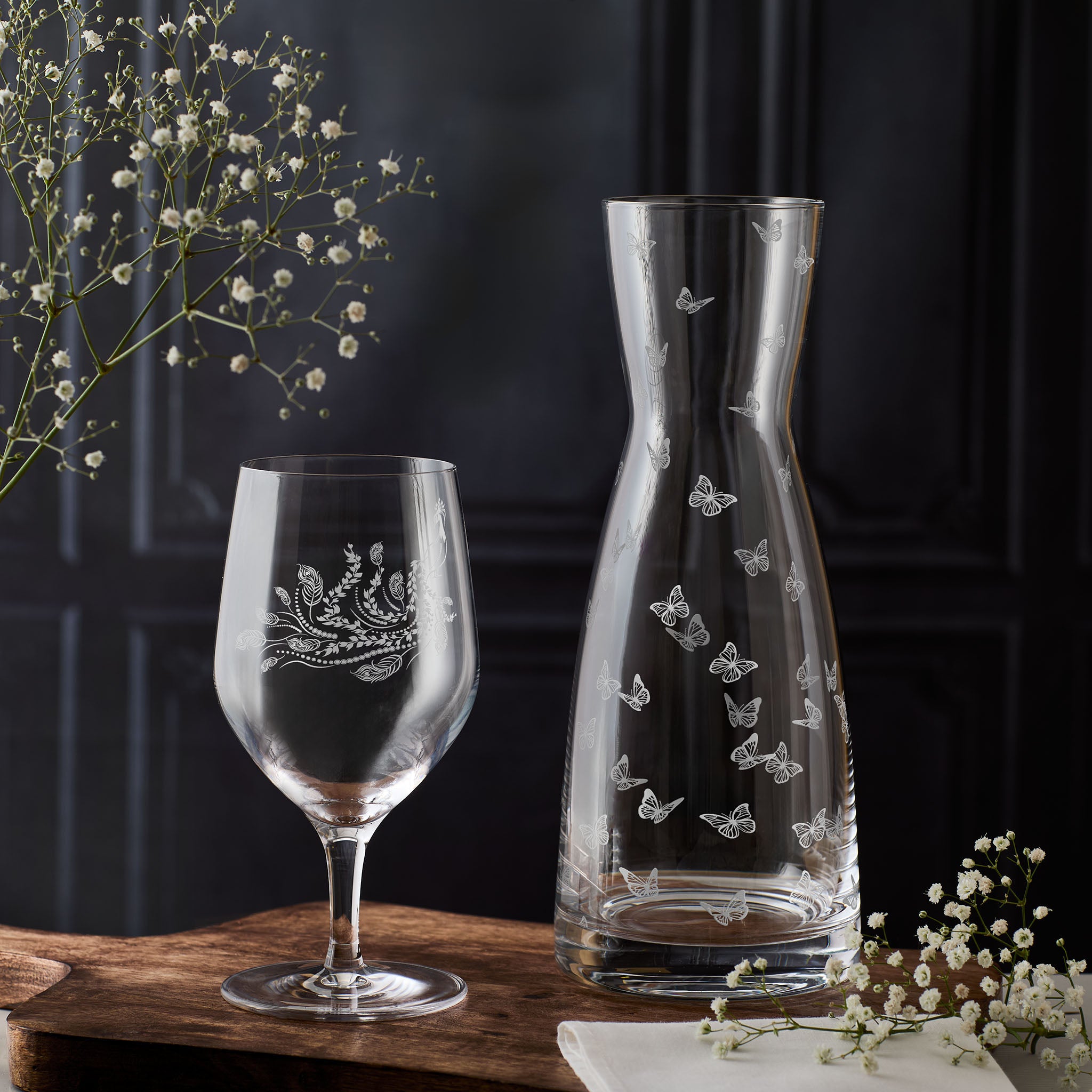 Engraved water glass and carafe with floral and butterfly designs on a dark background