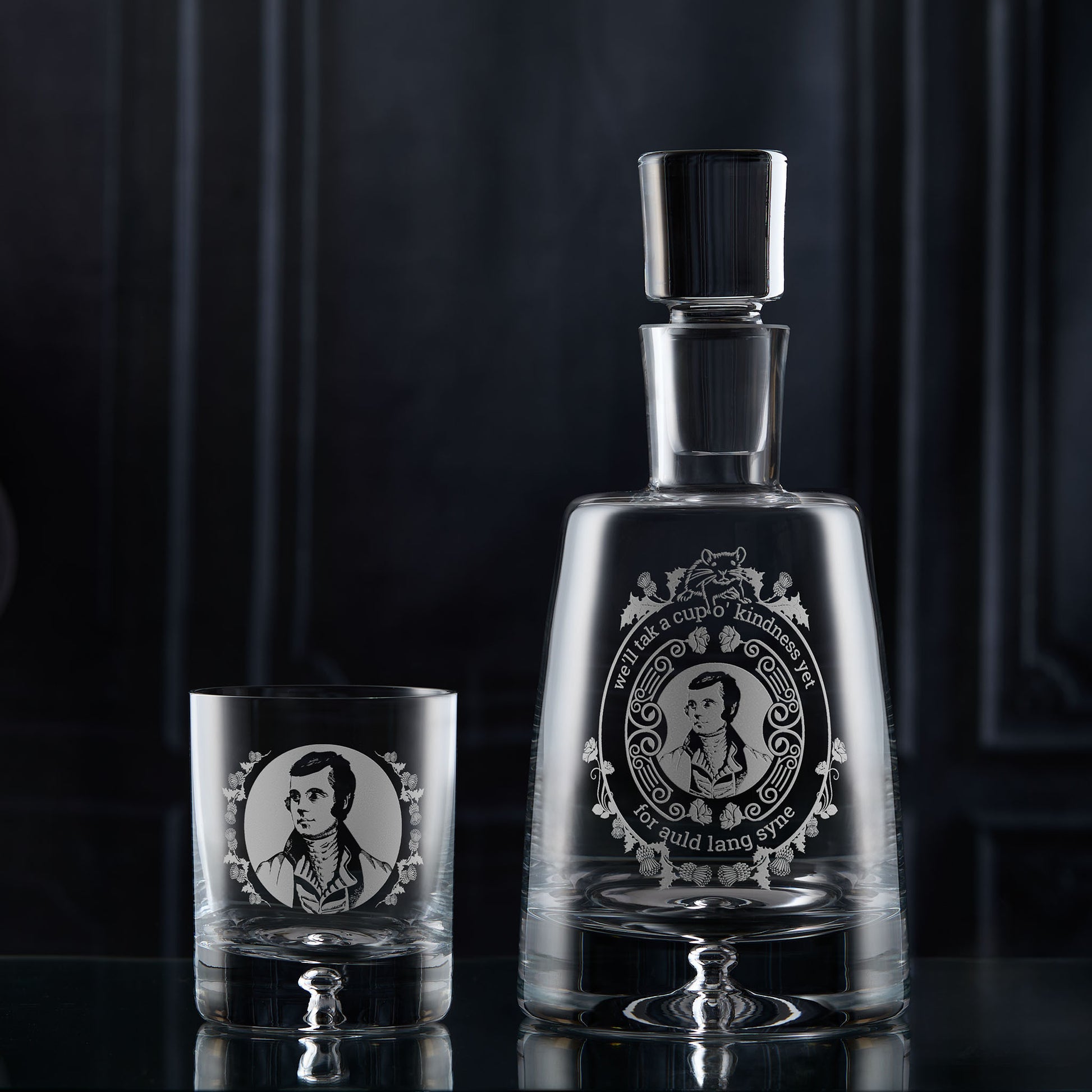 Glass decanter and whisky glass with an engraved portrait of Robert Burns on a dark background