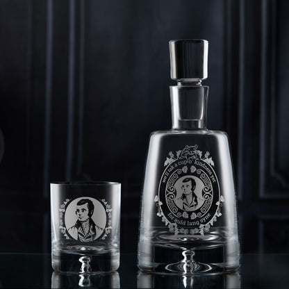 Glass decanter and whisky glass with an engraved portrait of Robert Burns on a dark background