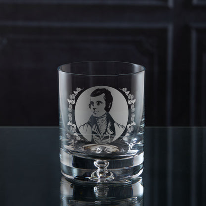 Clear glass tumbler with engraved portrait of the Scottish Poet Rabbie Burns on a dark surface