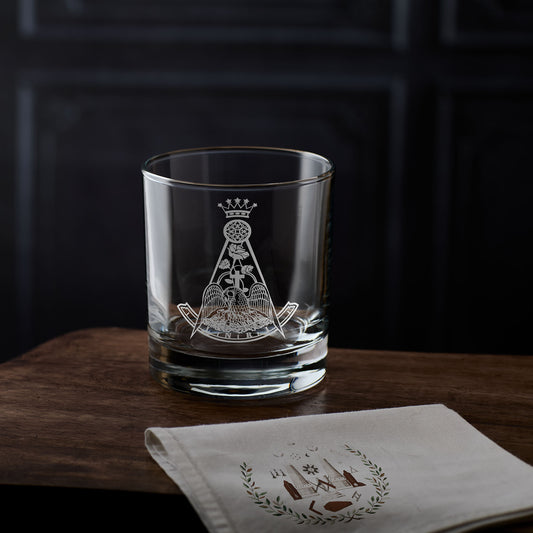 Whisky glass engraved with a rose croix design on a wooden surface with a dark background