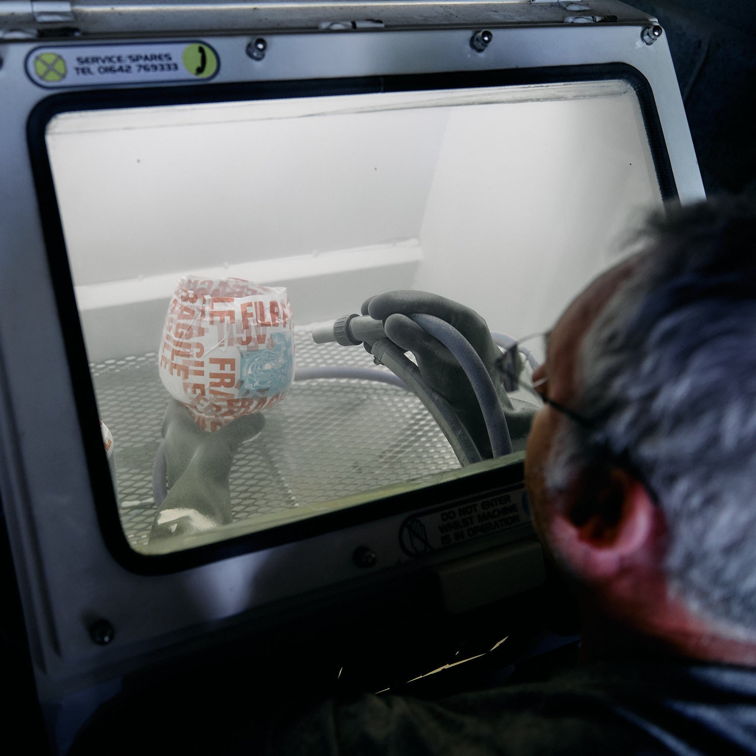 John engraving a glass by hand using high-pressure sandblasting, wearing protective gloves for safety and precision