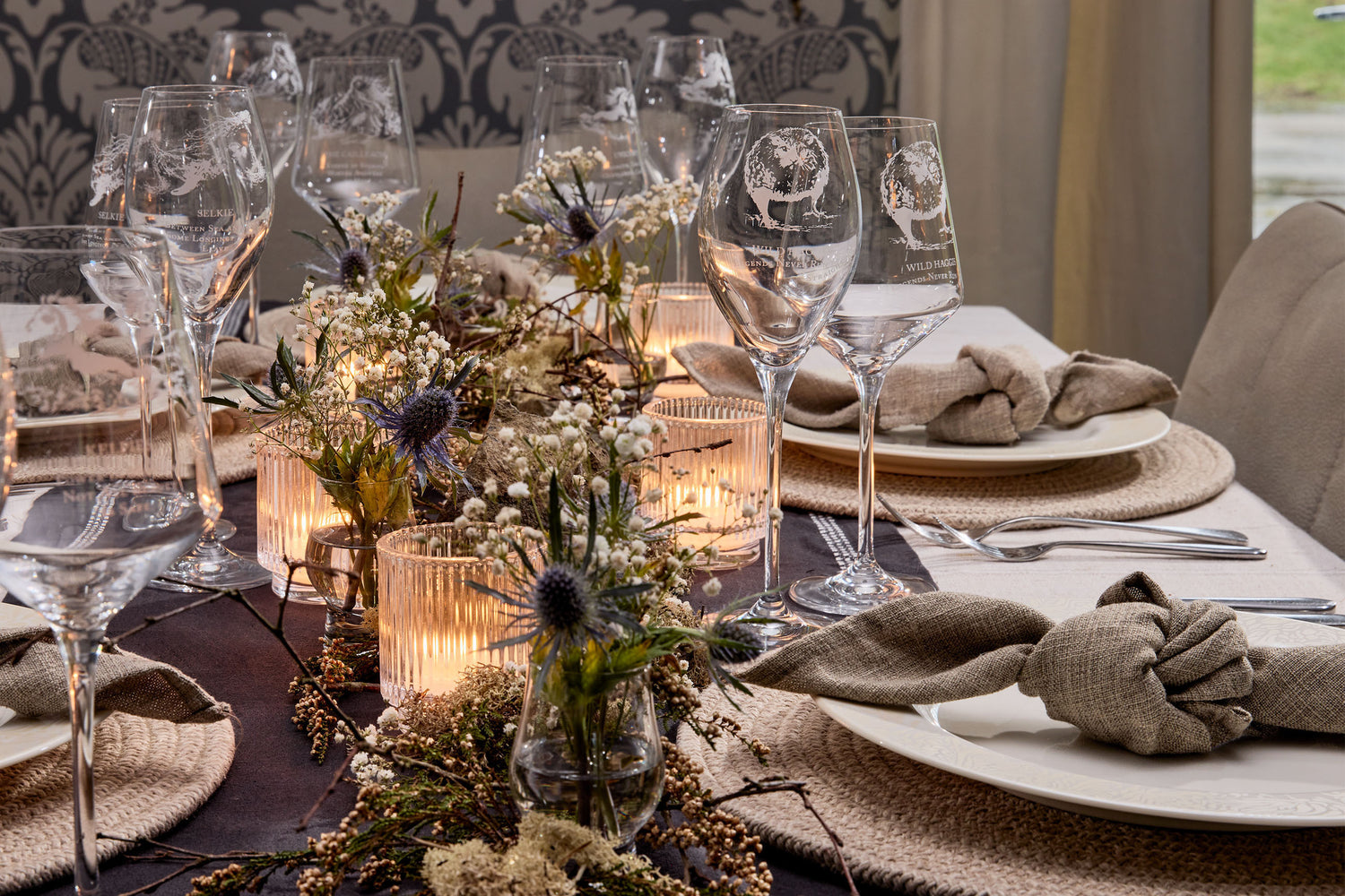 Elegant table setting with engraved wine glasses, candles, and decorative elements.