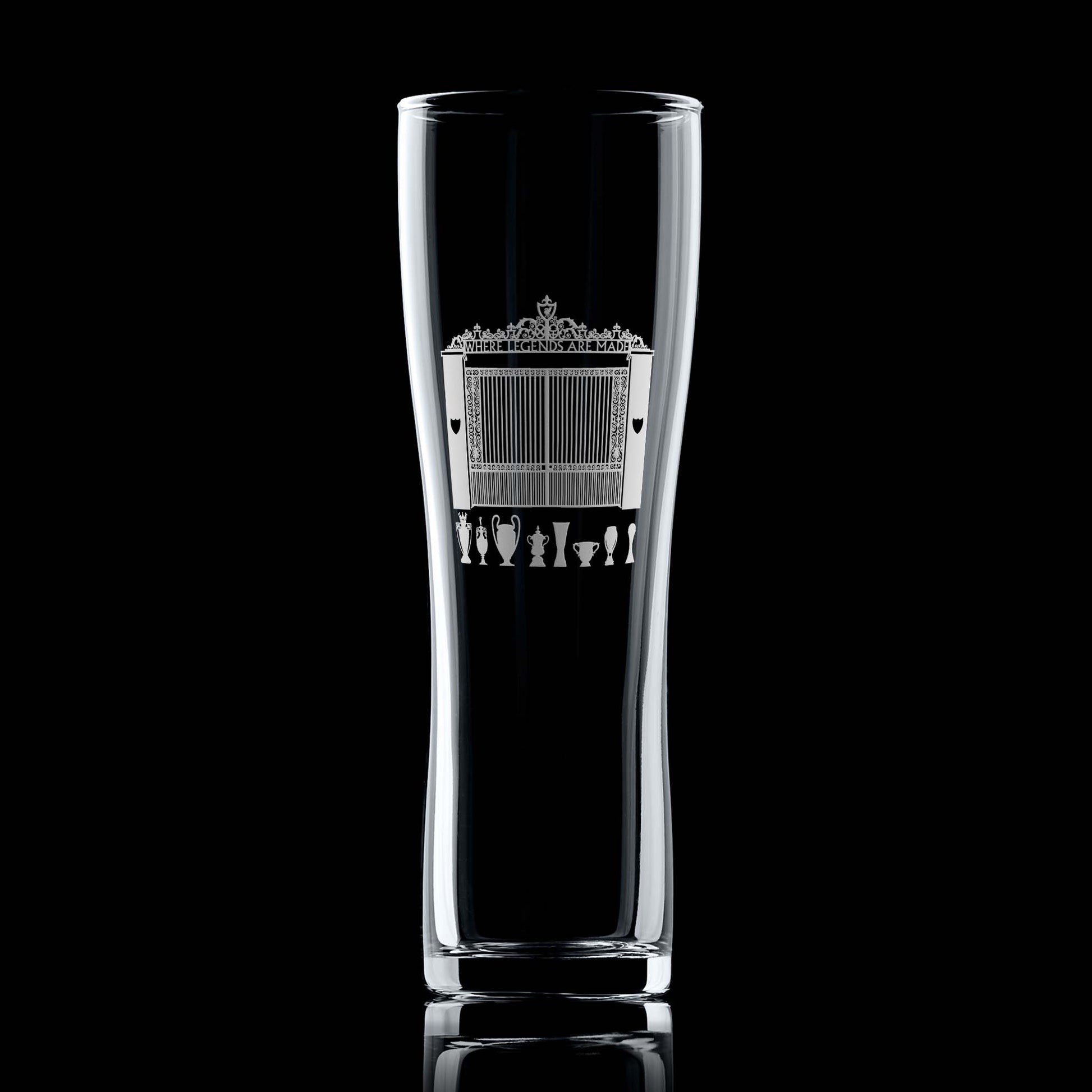 Engraved pint glass with Shankly Gates entrance to a Livepool football stadium and trophy silhouettes, shown front-facing on a black background.