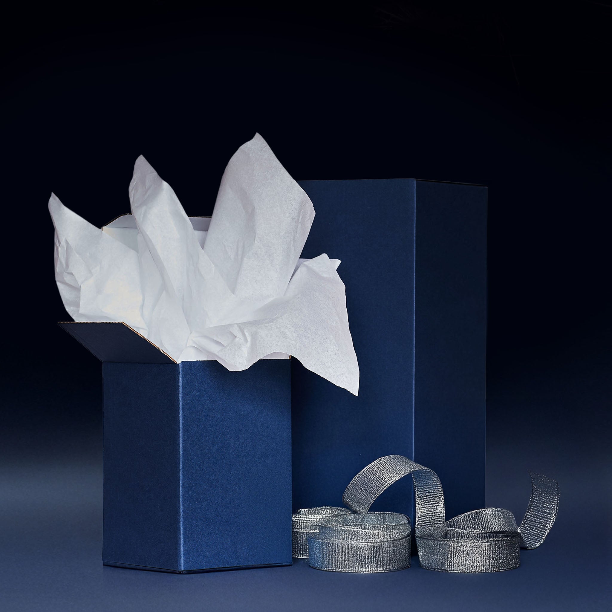Blue gift box with white tissue paper and silver ribbons on a dark background